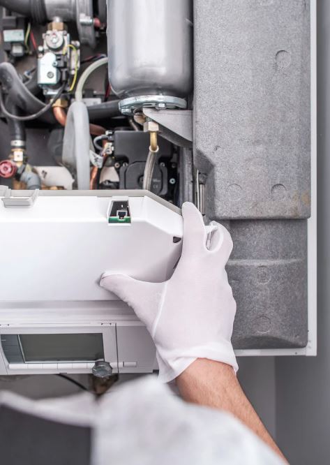 Technician in white gloves servicing a modern furnace unit.
