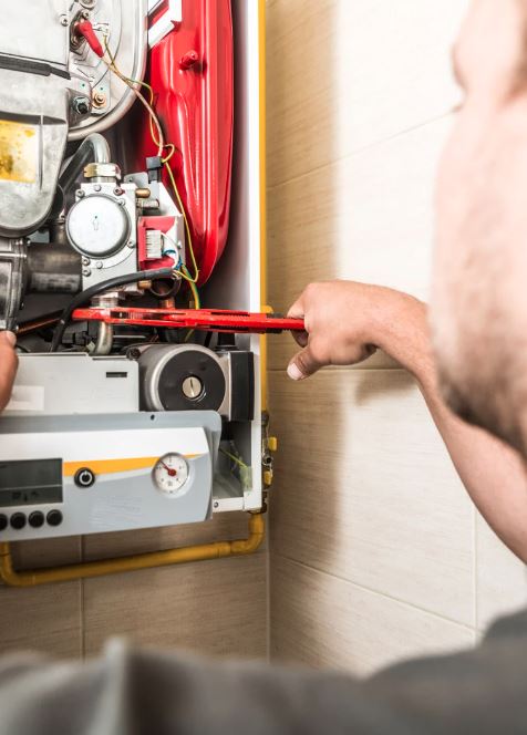 Technician using a wrench to repair a wall-mounted furnace.
