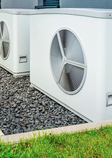 Outdoor heat pump unit installed on gravel base near a building.