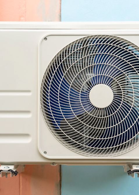 Close-up of a wall-mounted outdoor heat pump unit with a fan.