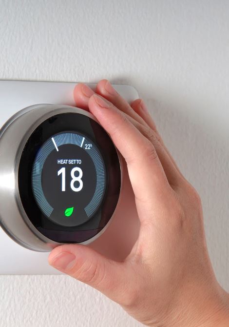 Hand adjusting a smart thermostat set to 18 degrees Celsius.