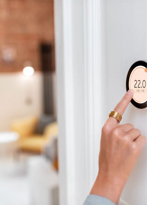 Person setting a wall-mounted smart thermostat to 22 degrees Celsius.