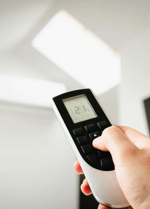 Hand holding a remote control set to 21 degrees Celsius.